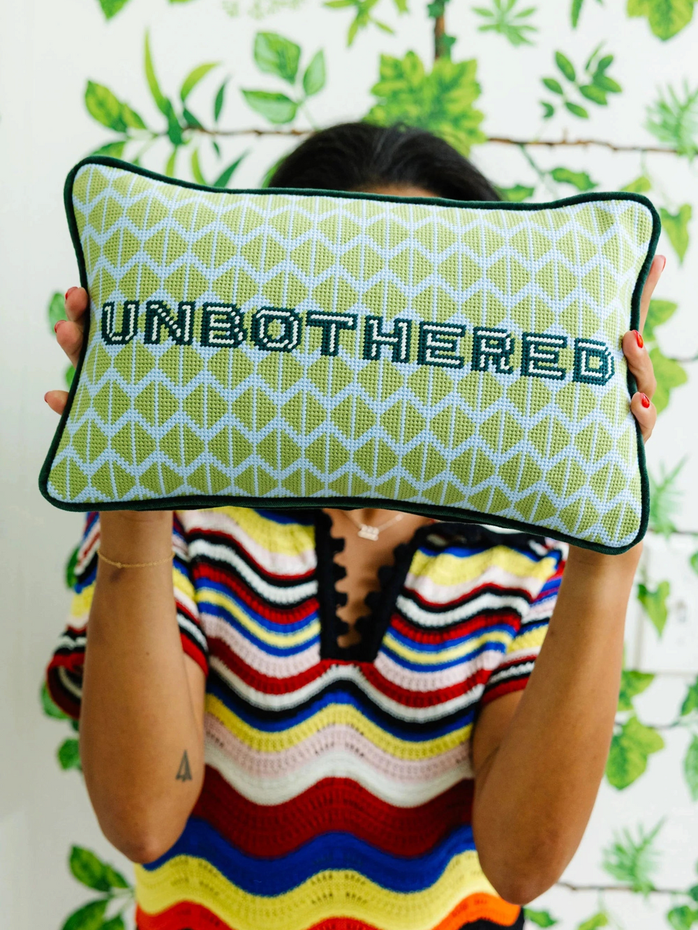Ileana Makri Unbothered needlepoint pillow with green geometric pattern and velvet backing held by a person