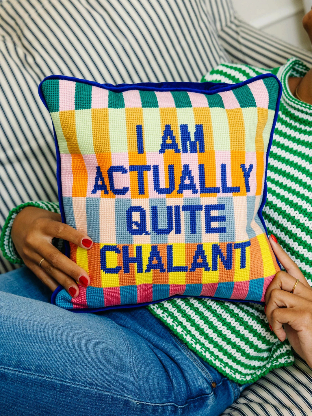 Ileana Makri Chalant needlepoint pillow with colorful checkered pattern and text held by a person in a striped sweater.