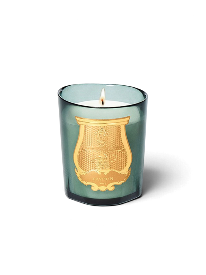 Ileana Makri Cire Trudon Figuerie candle in a green glass vessel with a gold emblem, emitting a warm fig fragrance.