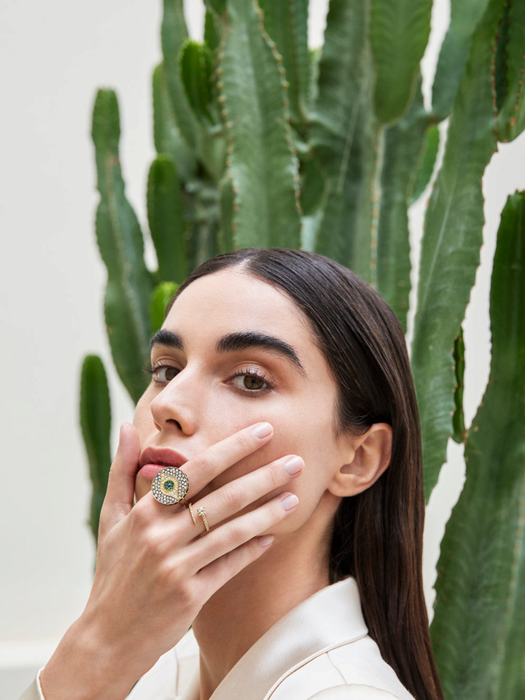 Ileana Makri Dawn Candy ring in 18k yellow gold with emeralds, diamonds, and sapphire, worn by a model near a cactus.