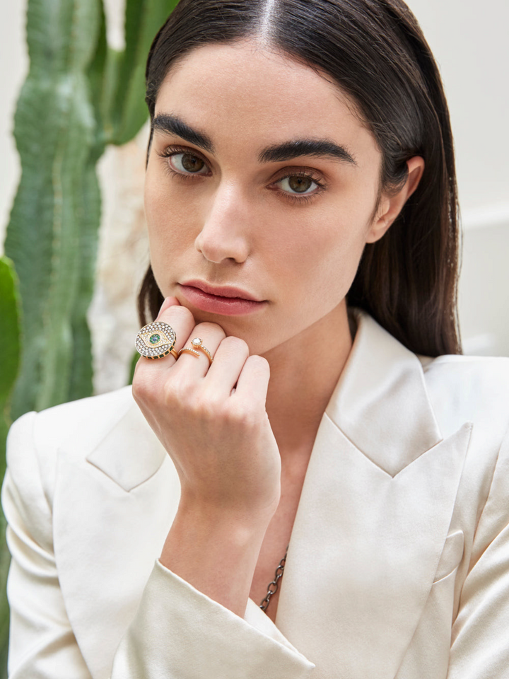 Model wearing an Ileana Makri Dawn Candy Ring in 18k yellow gold with emeralds, diamonds, and a central blue sapphire.