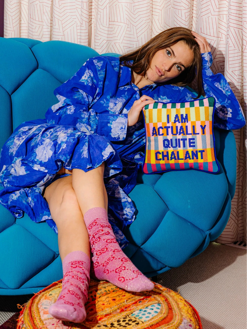 Ileana Makri Chalant needlepoint pillow with colorful stripes and text held by a woman on a blue tufted sofa