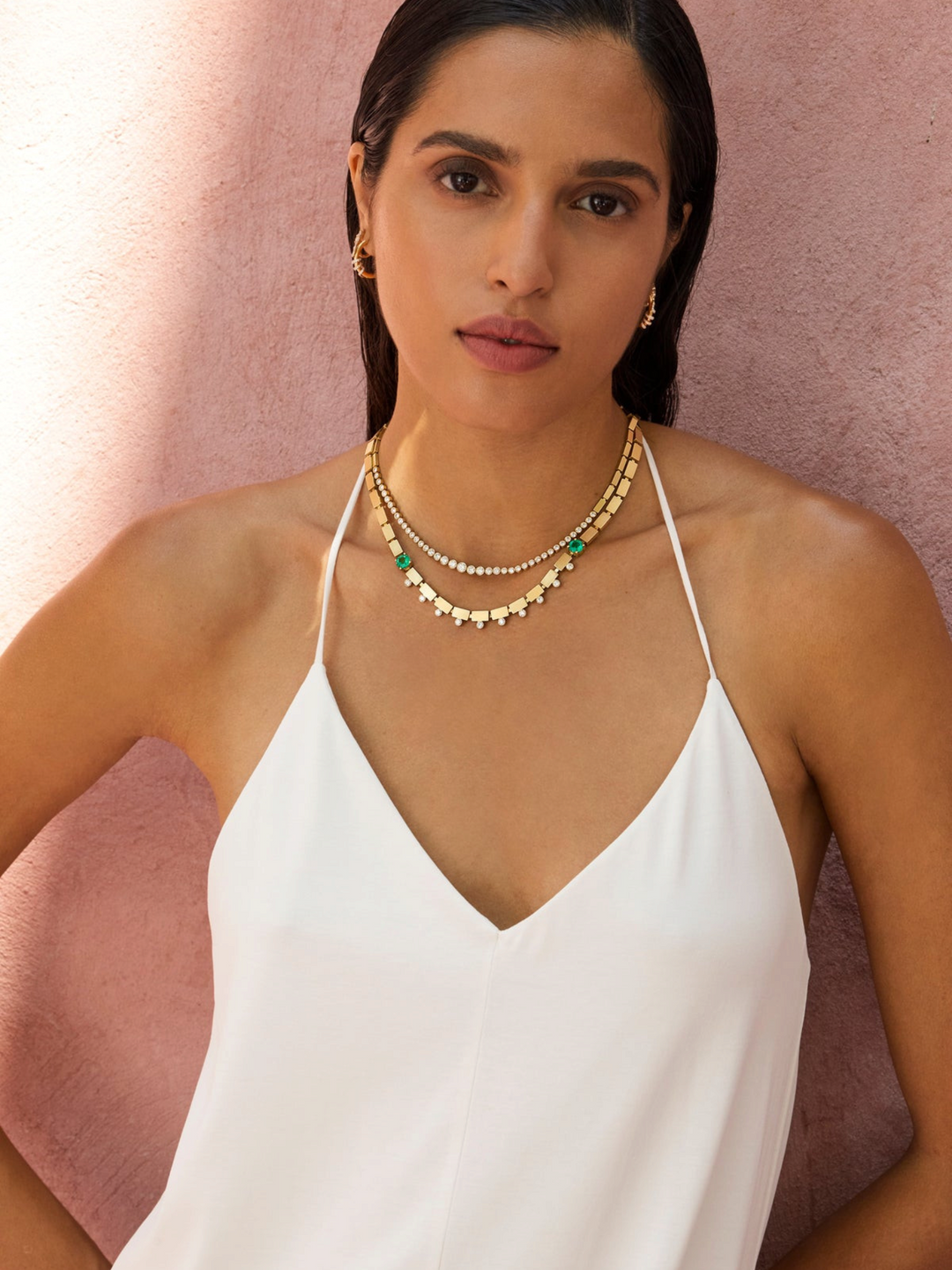 Model wearing Ileana Makri River Dew Necklace in 18k yellow gold with emeralds and diamonds against a pink wall