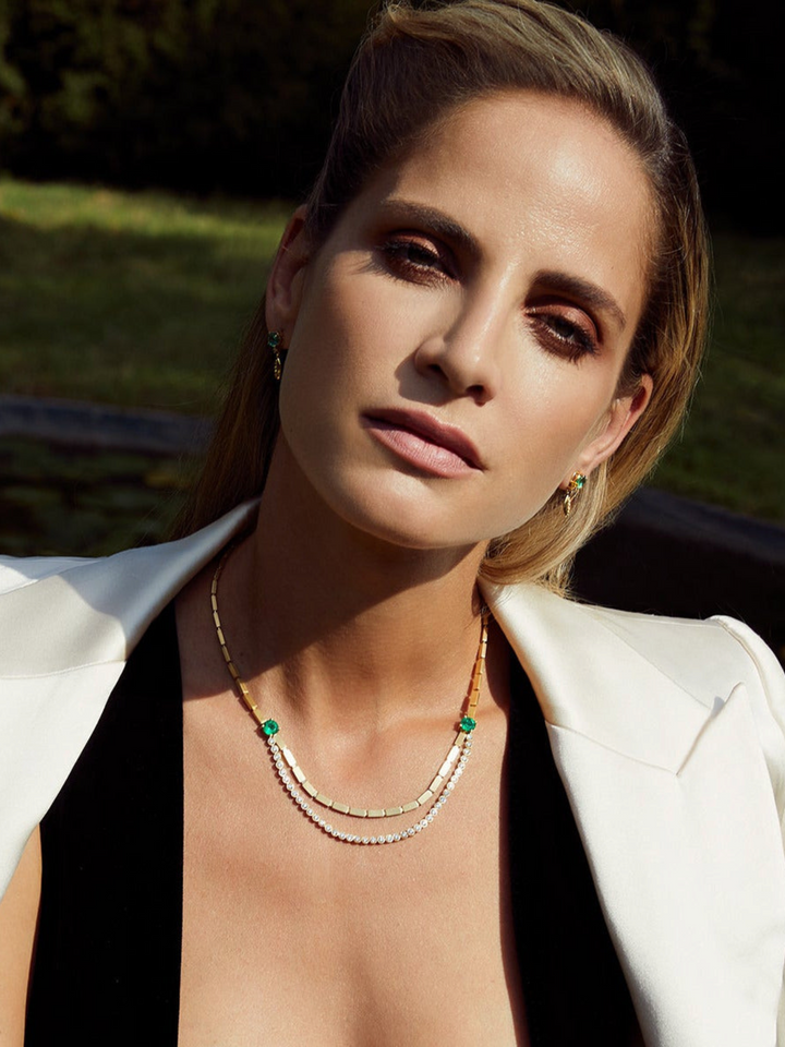 Ileana Makri Double Stream necklace in 18K yellow gold with emeralds and diamonds worn by a woman in a white blazer