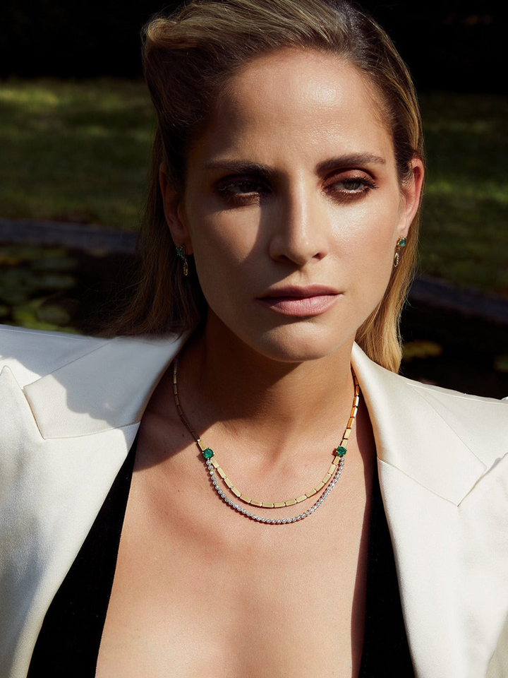 Ileana Makri Double Stream necklace in 18K yellow gold with emeralds and diamonds worn by a woman in a white blazer.