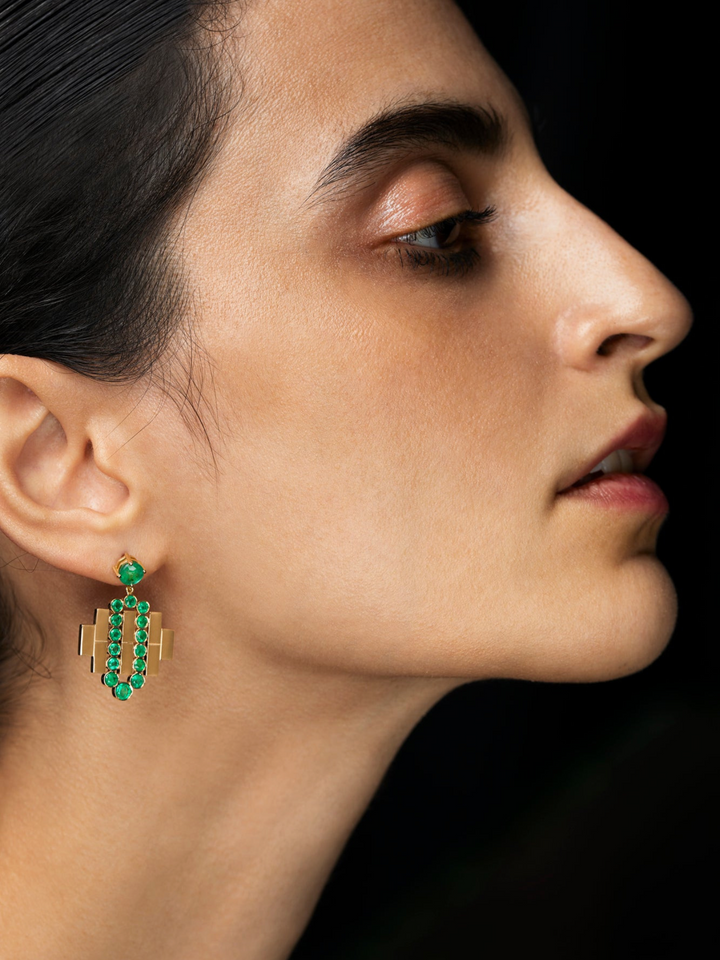 Ileana Makri Emerald Flow Bridge earrings in 18K yellow gold worn by a model, featuring vivid green emerald stones.