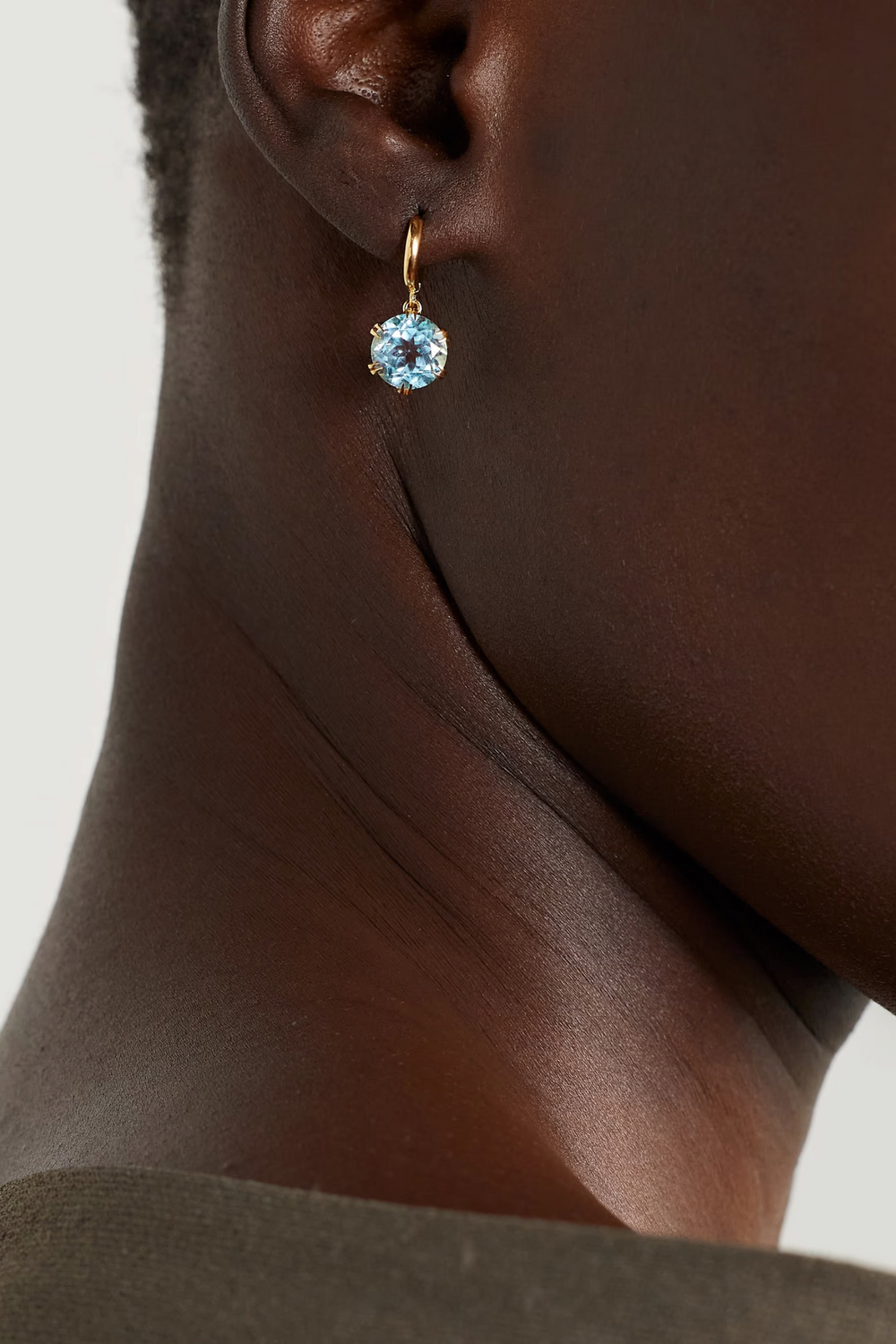 Ileana Makri 18k yellow gold midi hoop earrings featuring a dangling blue topaz stone in a crown setting on a model