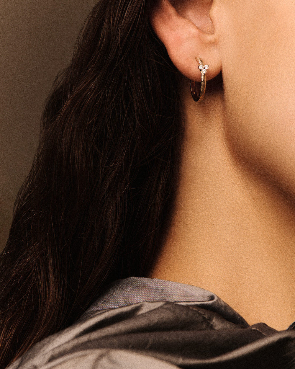 Close-up of a person wearing gold hoop earrings with a neutral background
