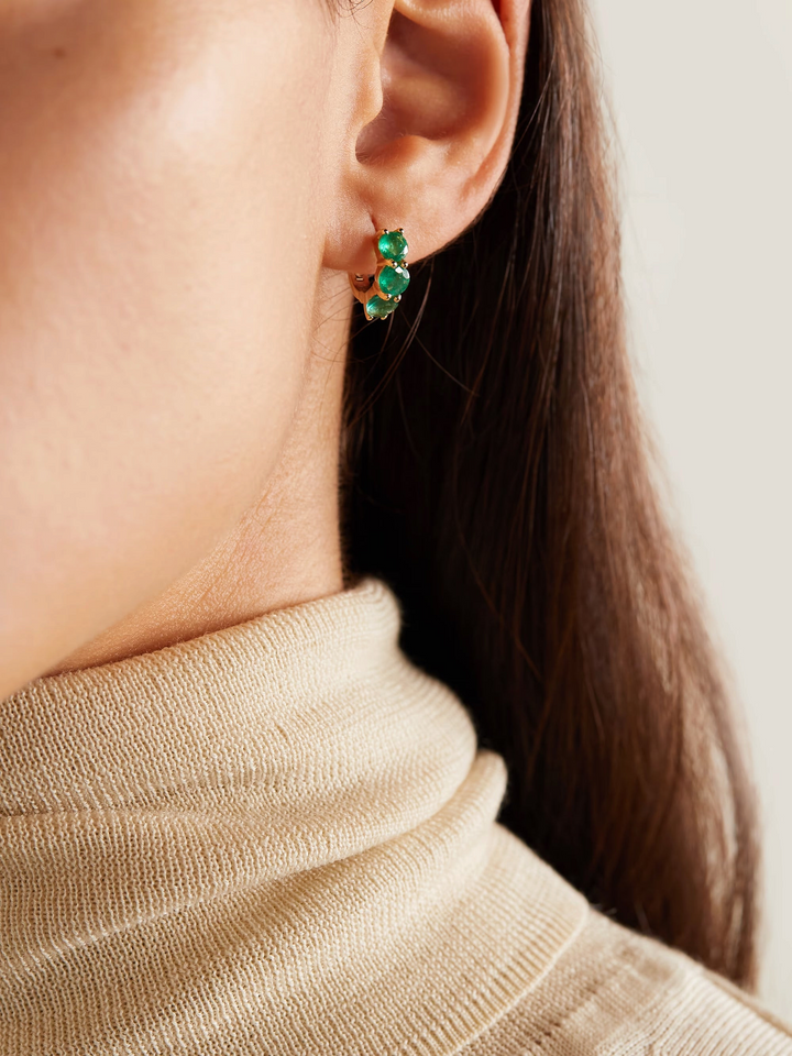 Ileana Makri 18k rose gold huggie hoop earrings featuring three vibrant green emeralds worn on a model