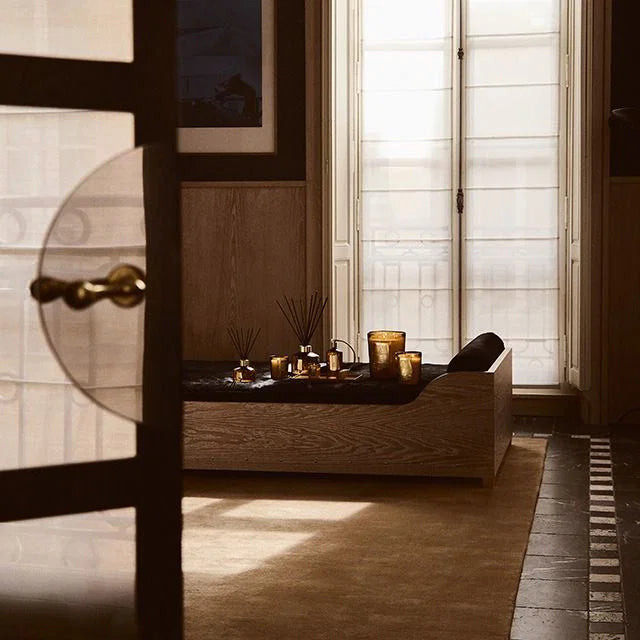 Ileana Makri Altair Oud and Peony candle set with amber glass vessels and reed diffusers on a wooden bench