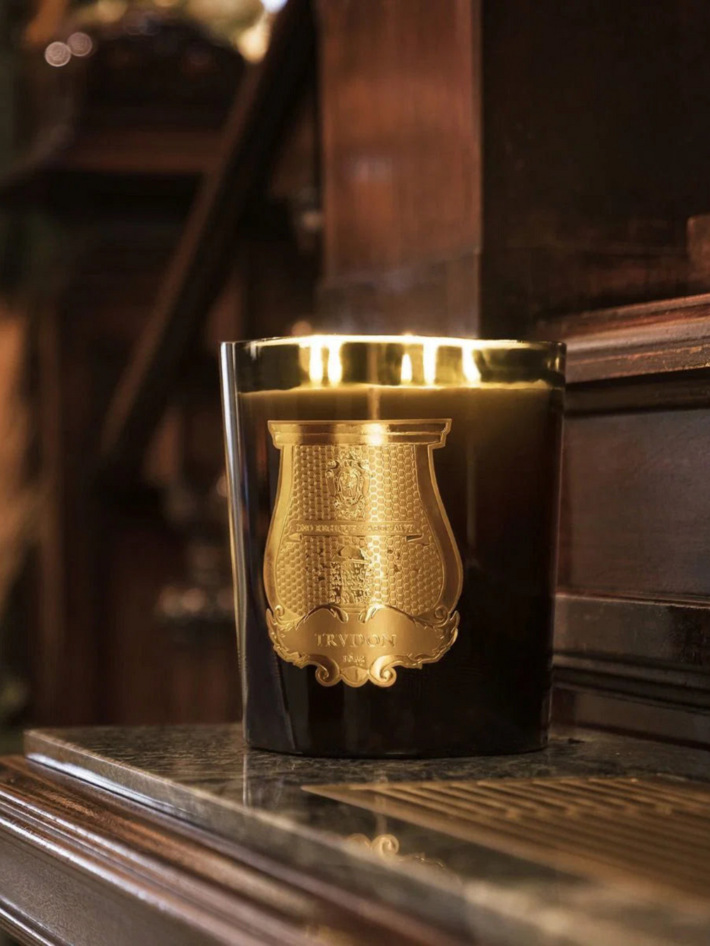 Ileana Makri Trudon Ernesto Grande candle in a dark glass vessel with a gold emblem, featuring five wicks.