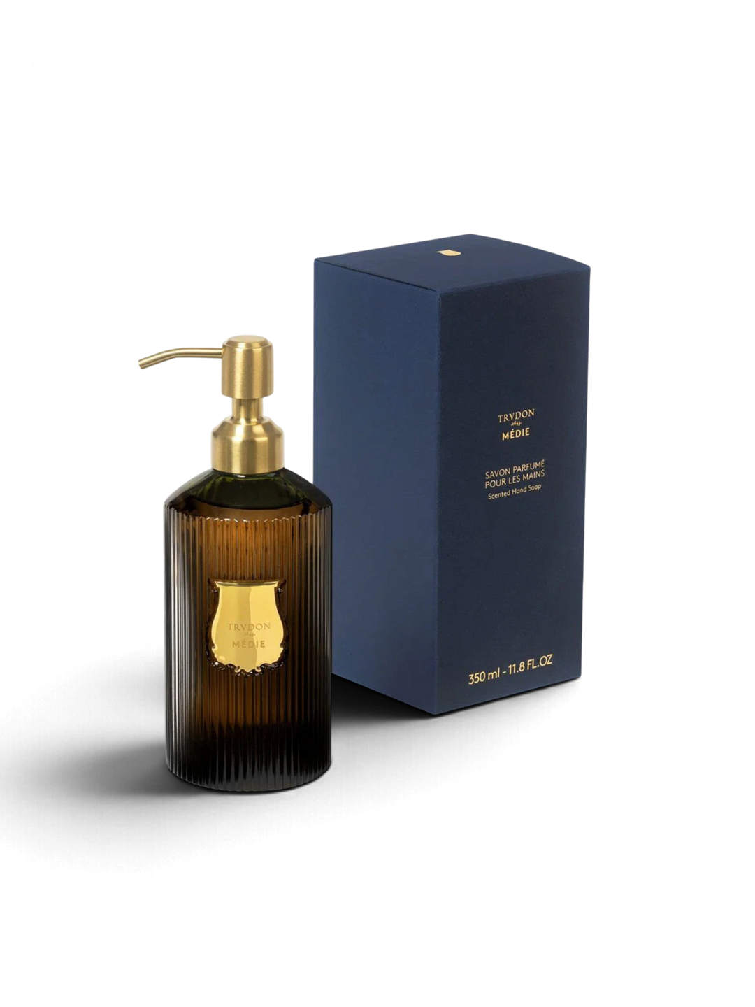 Ileana Makri Trudon Médie scented hand soap in a ribbed dark glass bottle with a gold pump next to its navy box.
