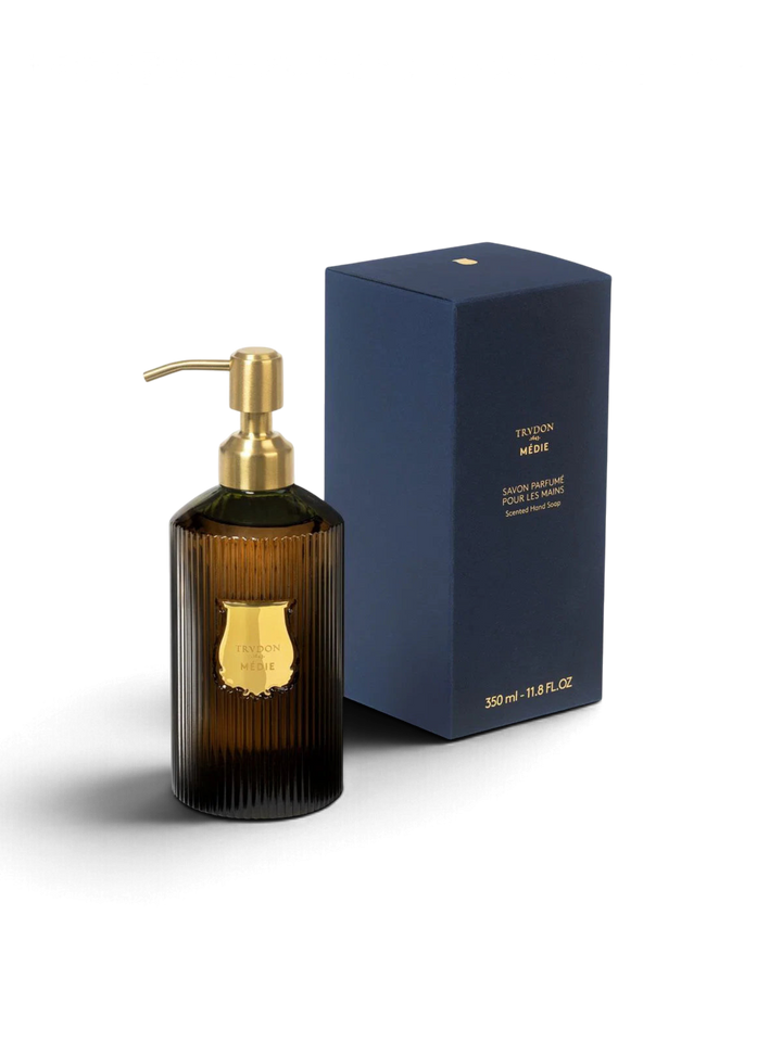 Ileana Makri Trudon Médie scented hand soap in a ribbed dark glass bottle with a gold pump next to its navy box.