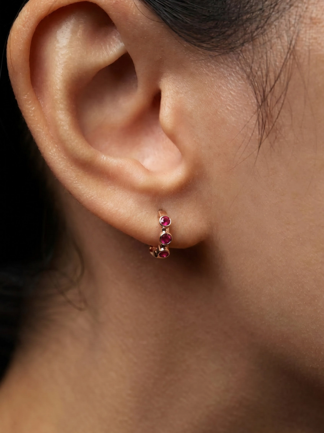 Ileana Makri Stepping Stone midi hoop earring in 18k rose gold featuring bezel-set rubies worn on a pierced earlobe.