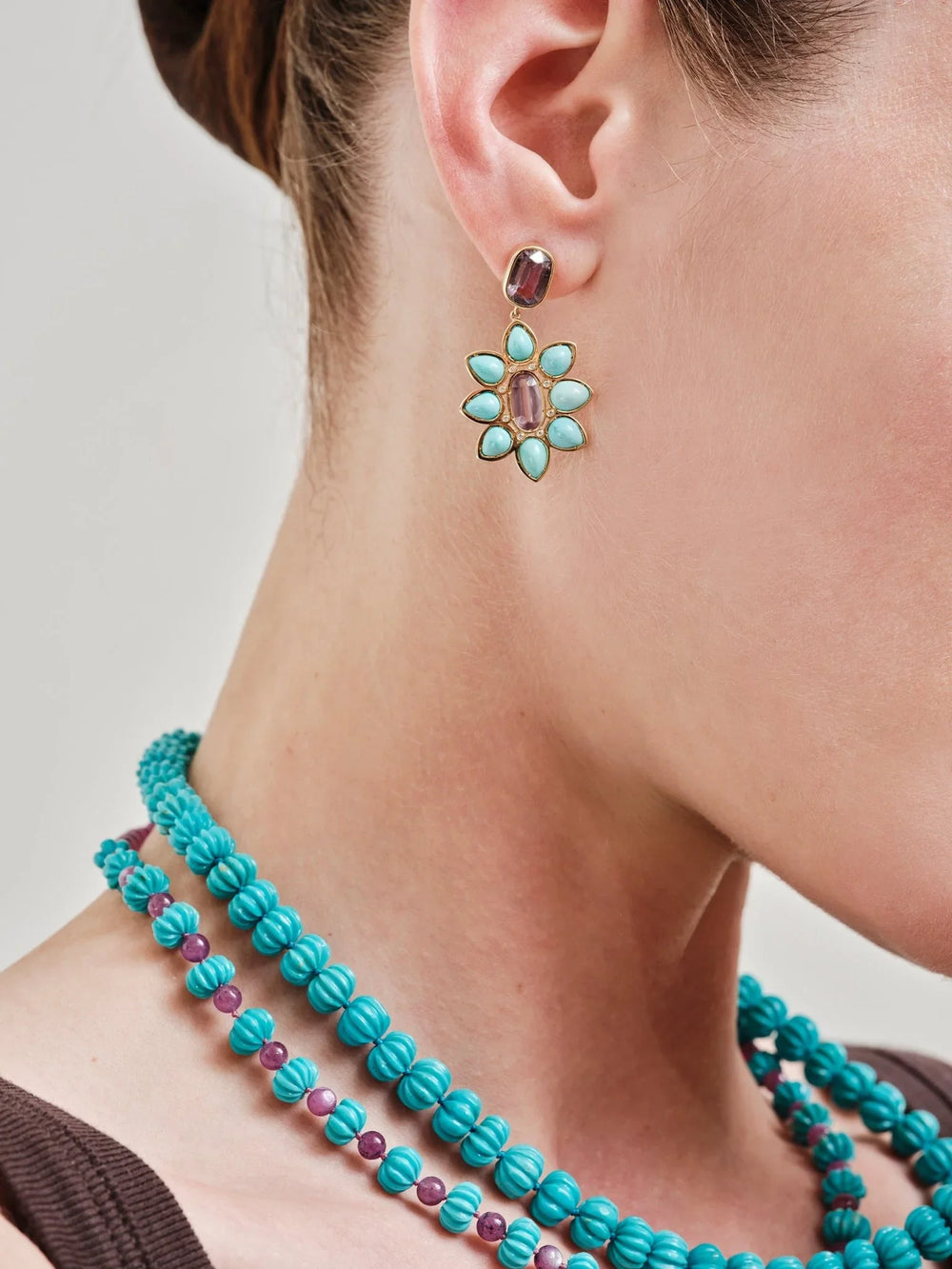 Turquoise and purple spinel drop earrings and layered turquoise bead necklaces on a woman